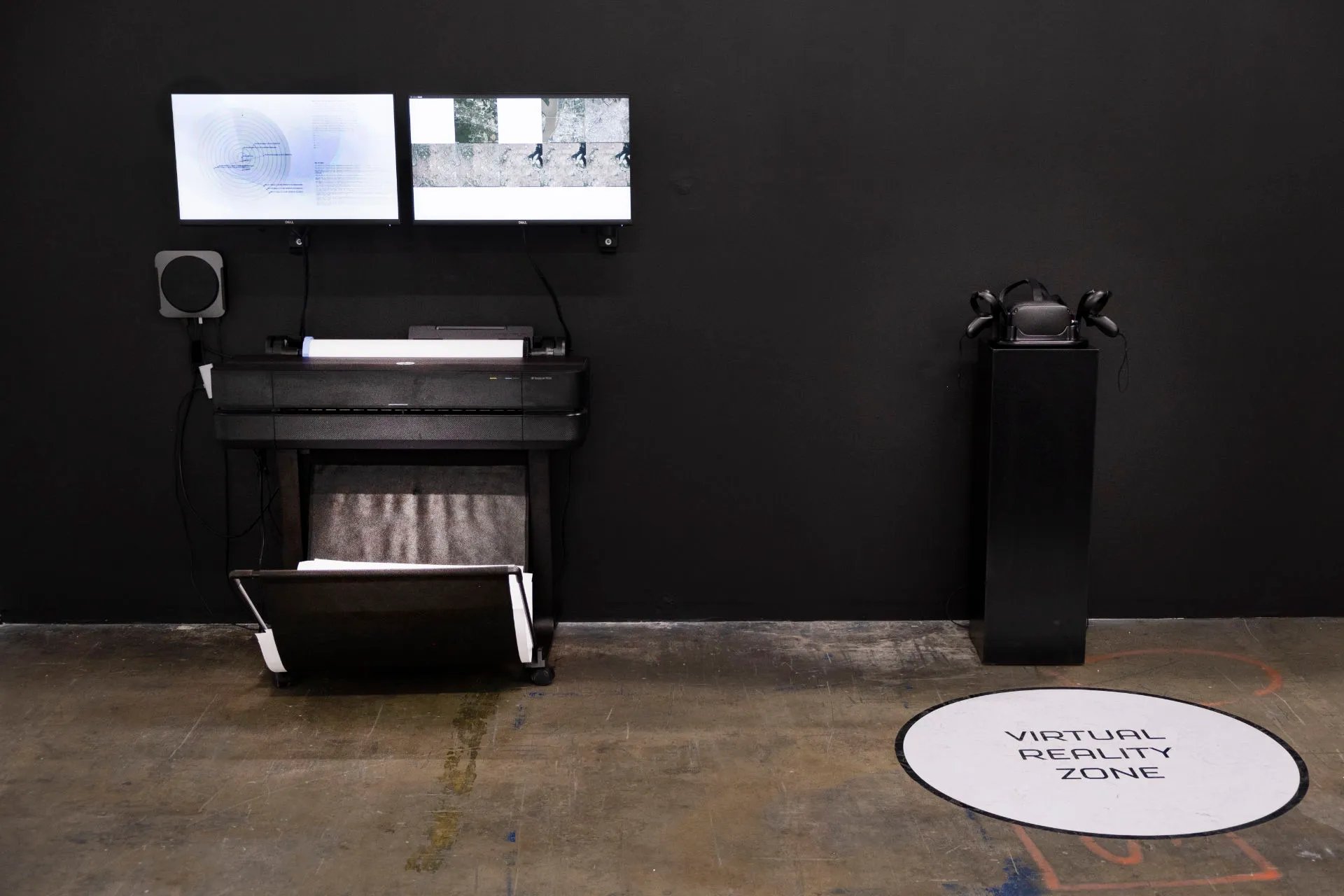 A room with two screens, a pedestal with an Oculus, and a circle on the floor in front of the Oculus that says Virtual Reality Zone