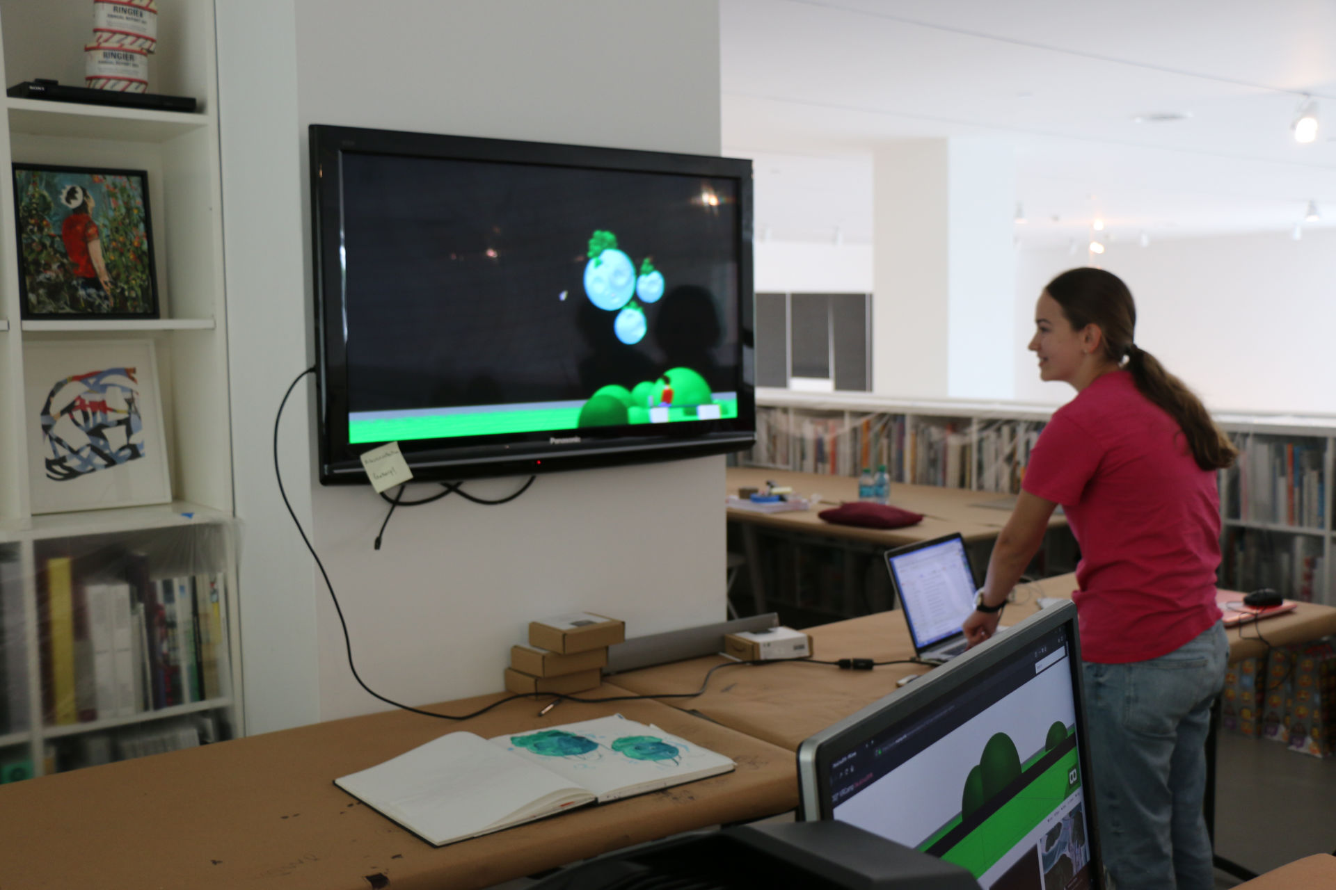 A girl smiling on a computer while her 3D artwork is on a screen